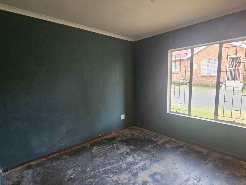 An empty bedroom featuring dark painted walls, a large window with security bars, and worn flooring, offering a blank canvas for renovation.