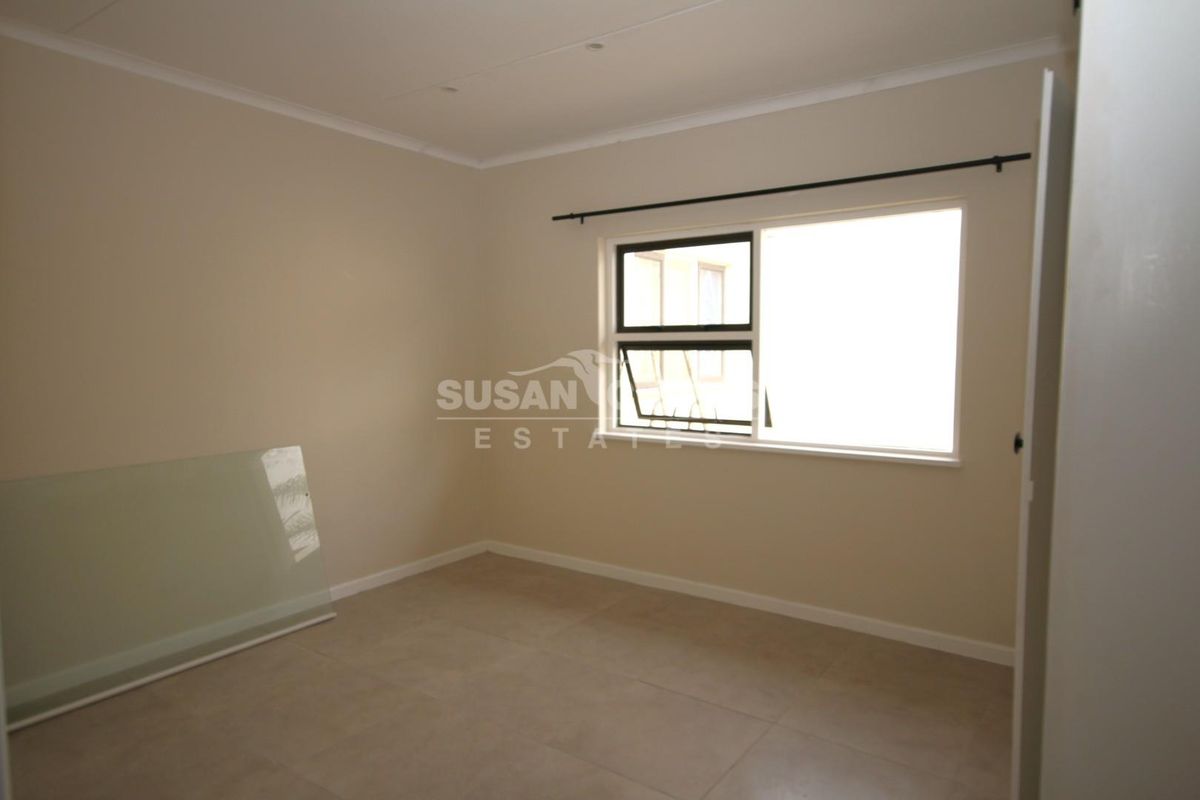 A clean, empty bedroom featuring neutral wall paint, tiled flooring, and an aluminium window frame with a fitted curtain rod.