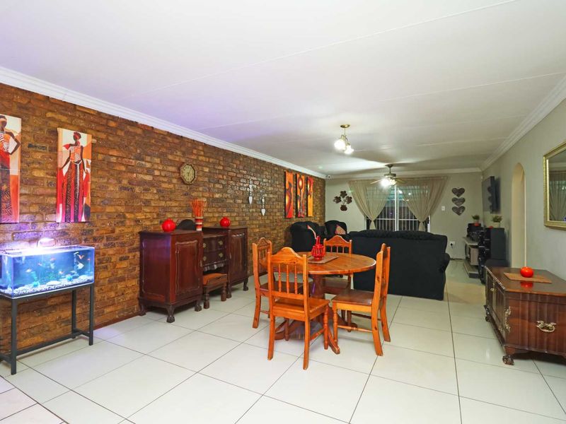 Spacious open-plan living and dining area featuring a prominent exposed brick feature wall, neutral tiled flooring, and ceiling fan lighting.