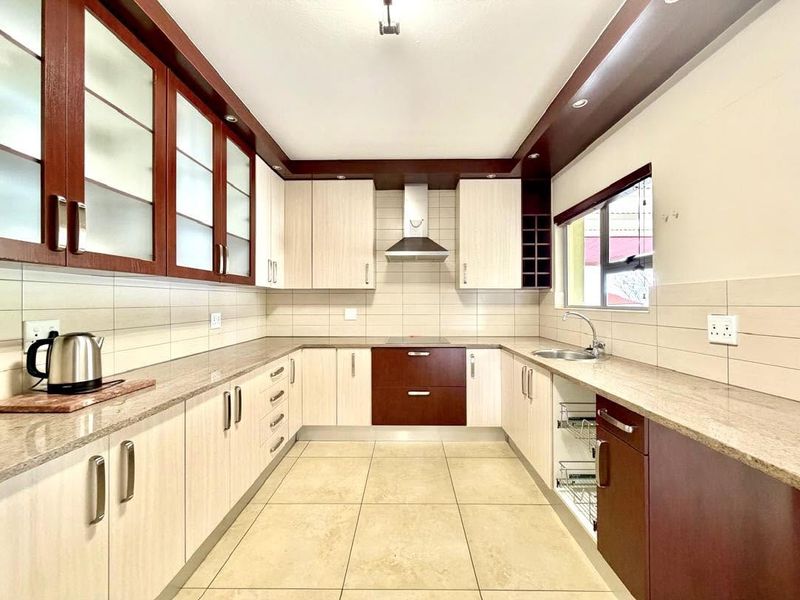 A well-maintained kitchen featuring granite countertops, ample built-in cabinetry, a stainless steel extractor fan, and neutral ceramic tile flooring.