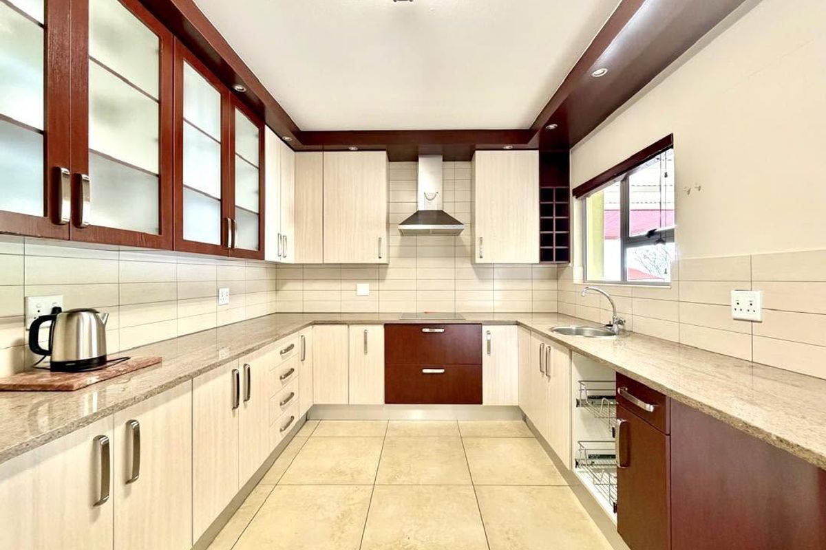 A well-maintained kitchen featuring granite countertops, ample built-in cabinetry, a stainless steel extractor fan, and neutral ceramic tile flooring.