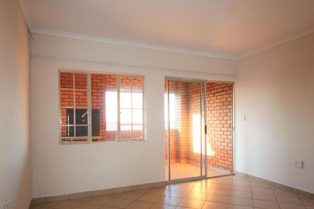 An empty living room featuring tiled flooring, a sliding glass door leading to a balcony, and exposed brick accents.