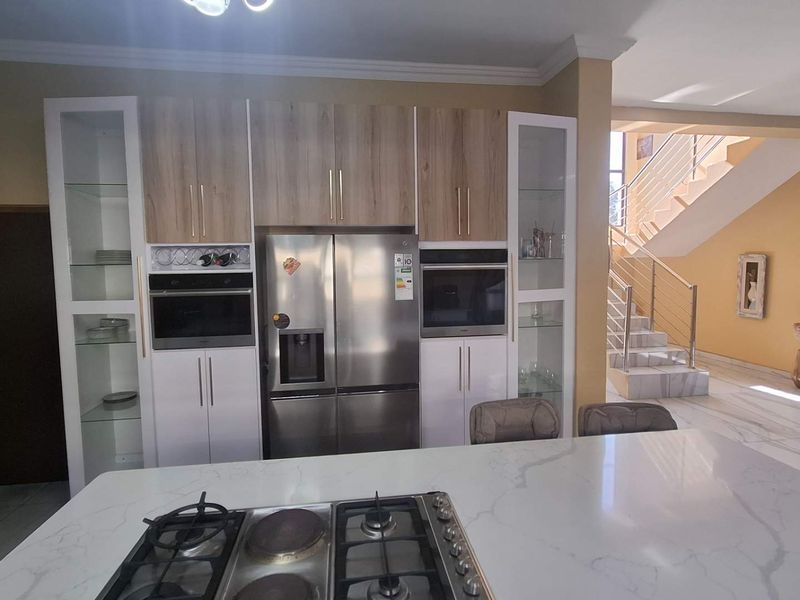 Modern kitchen featuring a central island with a gas hob, integrated appliances, and sleek cabinetry, flowing into an open-plan living area with a staircase.
