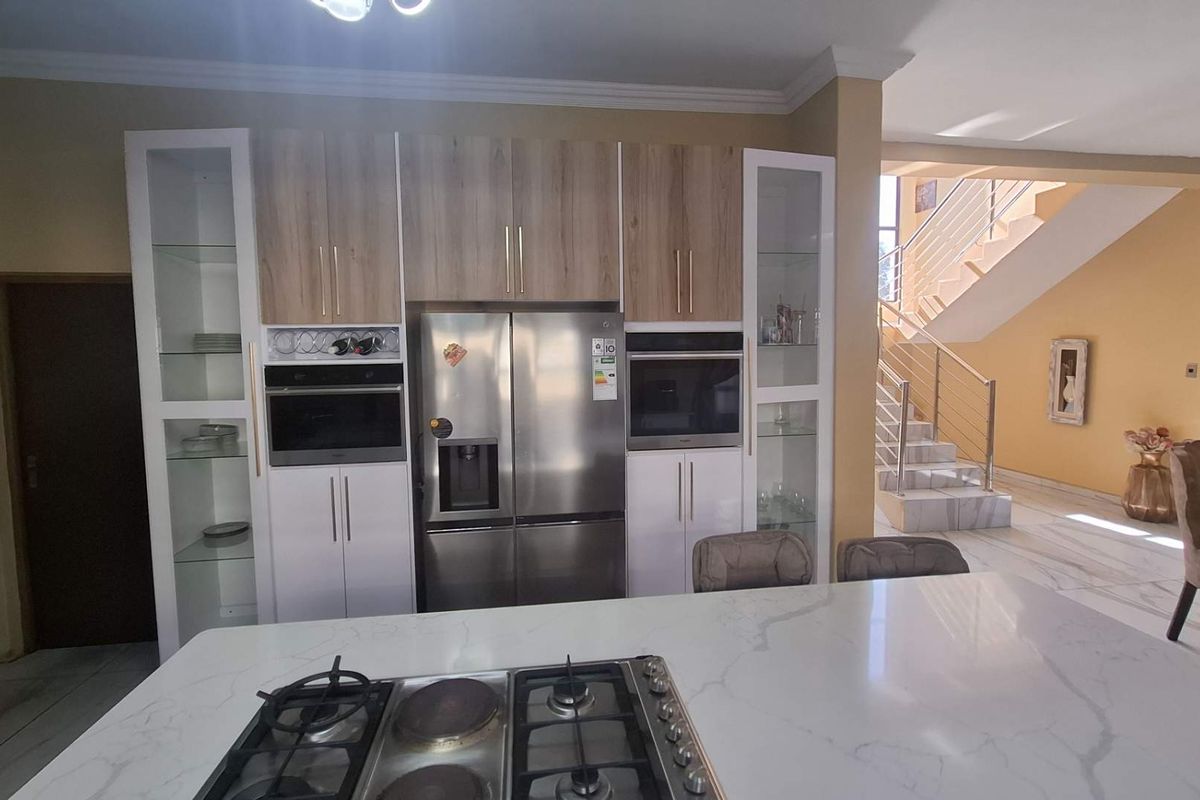Modern kitchen featuring a central island with a gas hob, integrated appliances, and sleek cabinetry, flowing into an open-plan living area with a staircase.
