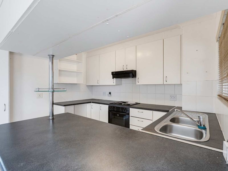 A functional kitchen featuring white cabinetry, dark laminate countertops, a double stainless steel sink, and built-in electric cooking appliances.