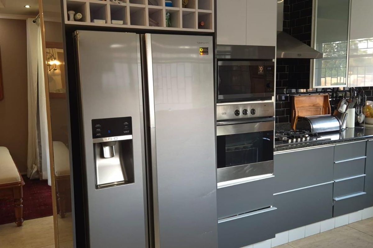 Modern kitchen featuring dark grey cabinetry, granite countertops, built-in oven, microwave, and stainless steel extractor fan, seamlessly flowing into the adjacent dining area.