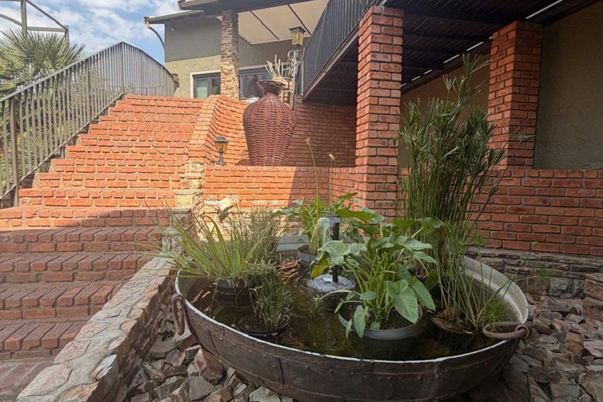 A rear exterior view featuring a brick staircase, stone-clad landscaping, and a covered patio area with brick support pillars.