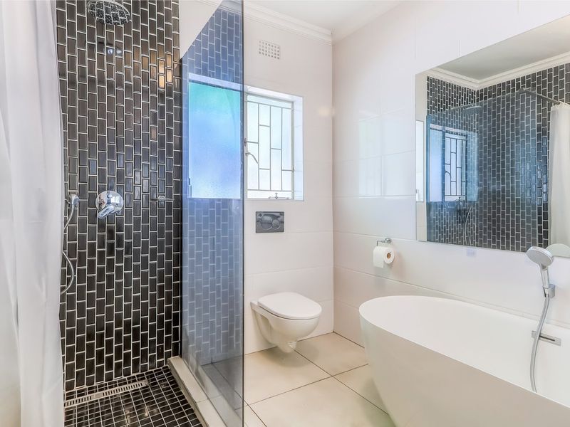 Modern bathroom featuring a sleek freestanding bathtub, a separate shower with dark subway tiling, and a wall-mounted toilet.