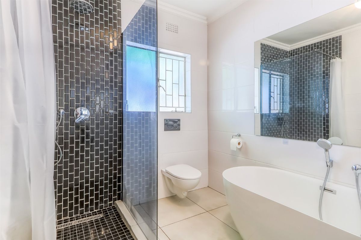 Modern bathroom featuring a sleek freestanding bathtub, a separate shower with dark subway tiling, and a wall-mounted toilet.