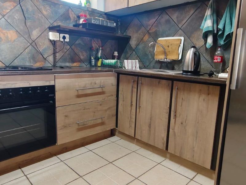A functional kitchen featuring wood-look cabinetry, a built-in oven, hob, and tiled backsplash with neutral floor tiles.