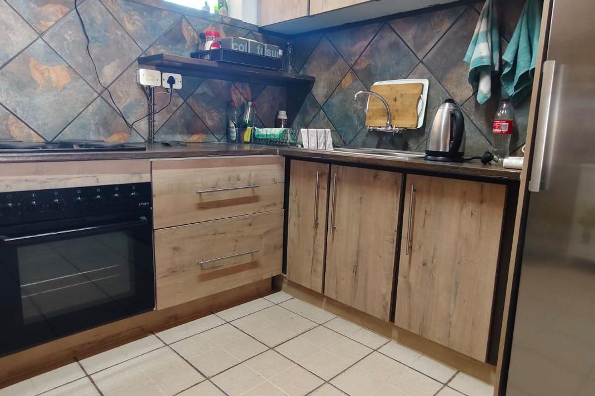 A functional kitchen featuring wood-look cabinetry, a built-in oven, hob, and tiled backsplash with neutral floor tiles.
