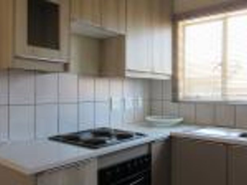 A functional kitchen featuring light wood-tone cabinetry, laminate countertops, a tiled backsplash, and integrated cooking appliances with a window for natural light.