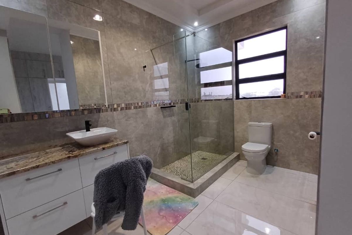 Modern bathroom featuring a glass-enclosed walk-in shower, stone-topped vanity with vessel sink, and large-format wall and floor tiles.