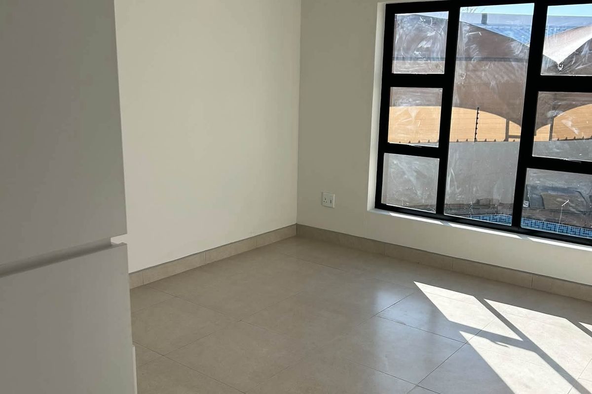 A bright, empty bedroom featuring neutral tiled flooring and a modern black aluminium window frame, offering a clean and versatile space.