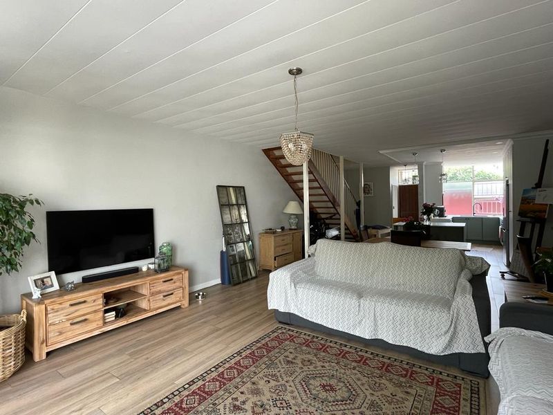 Open-plan living area featuring timber staircase, laminate flooring, and panelled ceiling, flowing into the kitchen space.