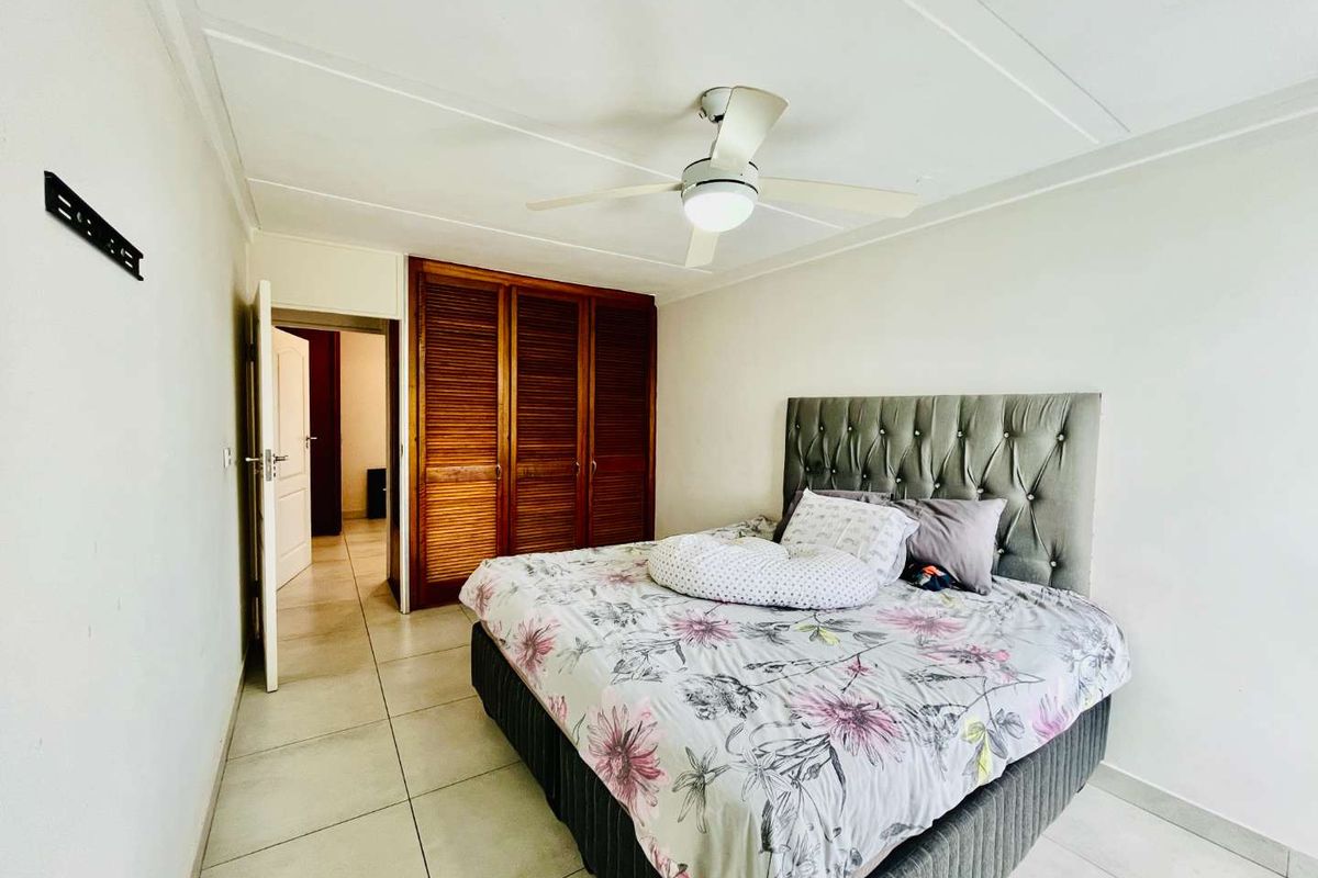 A bedroom featuring built-in wooden louvered cupboards, tiled flooring, and a ceiling fan, providing a functional and neutral living space.