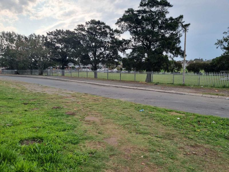 A street-level view showing the road, perimeter security fencing, and surrounding green space in the neighbourhood.