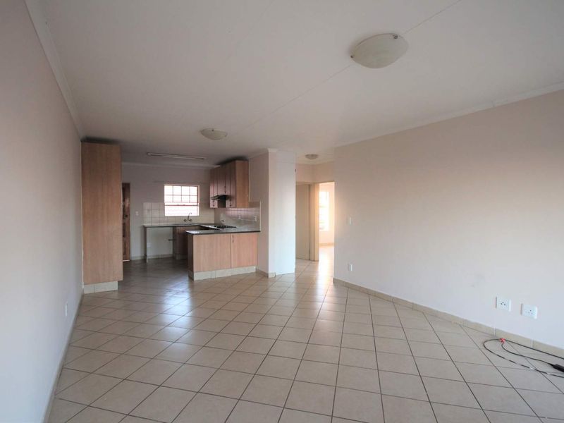 An open-plan living and kitchen area featuring tiled flooring, built-in cabinetry, and a functional kitchen layout in a neutral, well-maintained space.