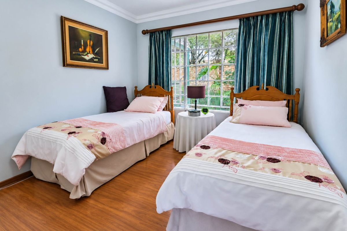 A well-maintained bedroom featuring laminate flooring, crown molding, and a window with security bars, offering a bright and comfortable living space.