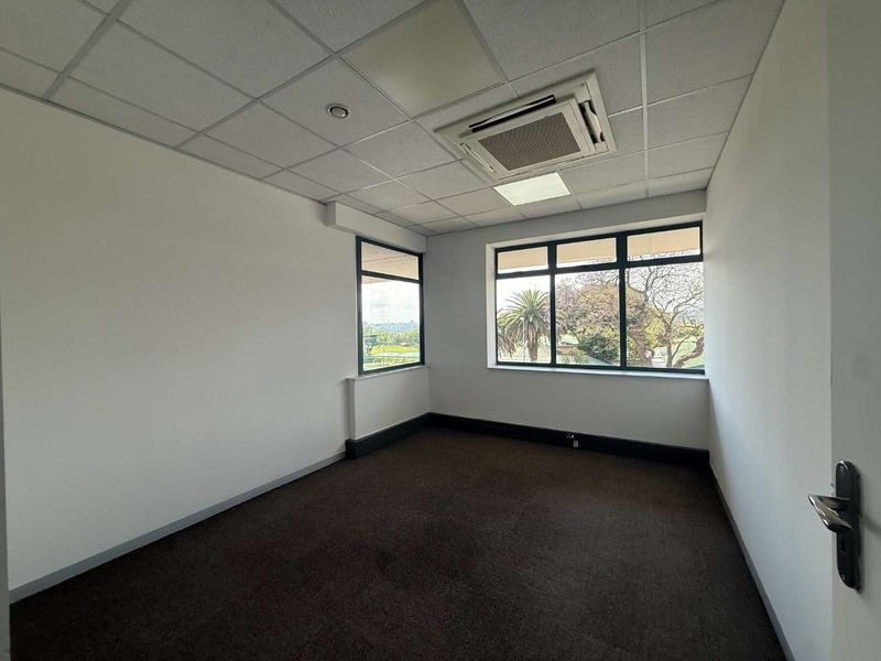 A bright, empty office space featuring a suspended ceiling, integrated air conditioning, and large windows providing natural light and exterior views.