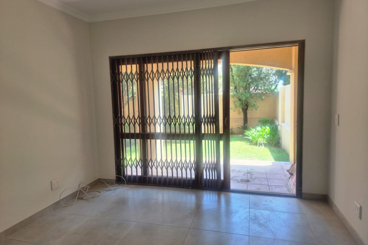 An empty living room featuring tiled flooring and a sliding glass door with a security gate, providing direct access to a private garden patio.