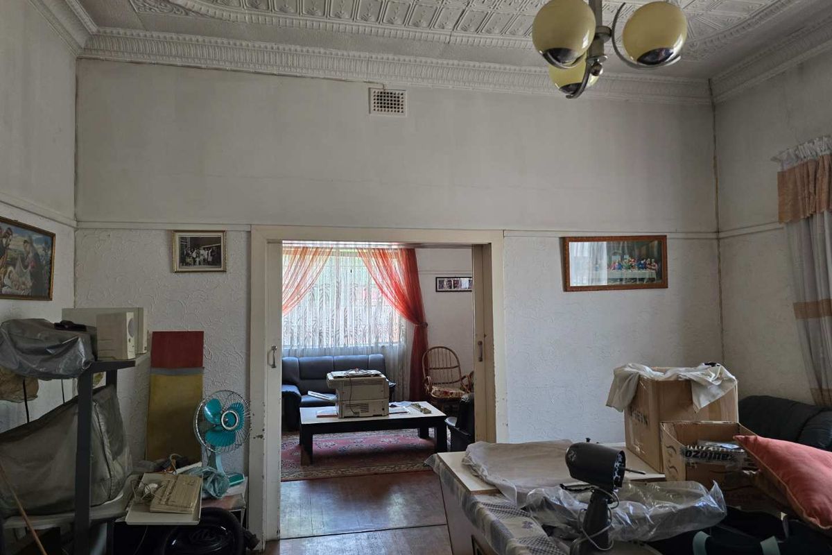 A living room featuring traditional ornate pressed metal ceilings, timber flooring, and an open doorway leading to an adjoining living space.
