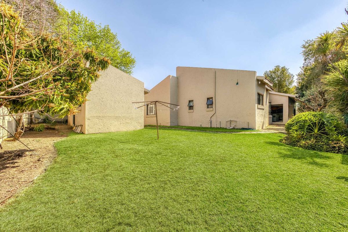 A view of the rear exterior of the house featuring a well-maintained lawn, stucco walls, and established garden landscaping.
