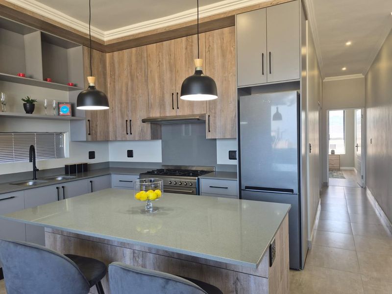 Modern kitchen featuring wood-grain and grey cabinetry, stone countertops, a central island, gas hob, and stylish pendant lighting in an open-plan layout.