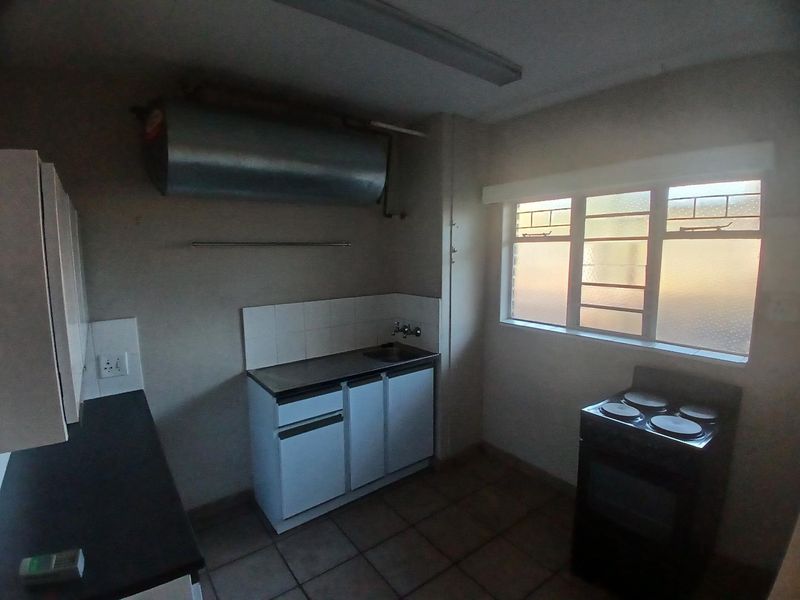 A functional kitchen featuring built-in cabinetry, a stainless steel sink, tiled flooring, and an electric stove, with an exposed geyser unit.