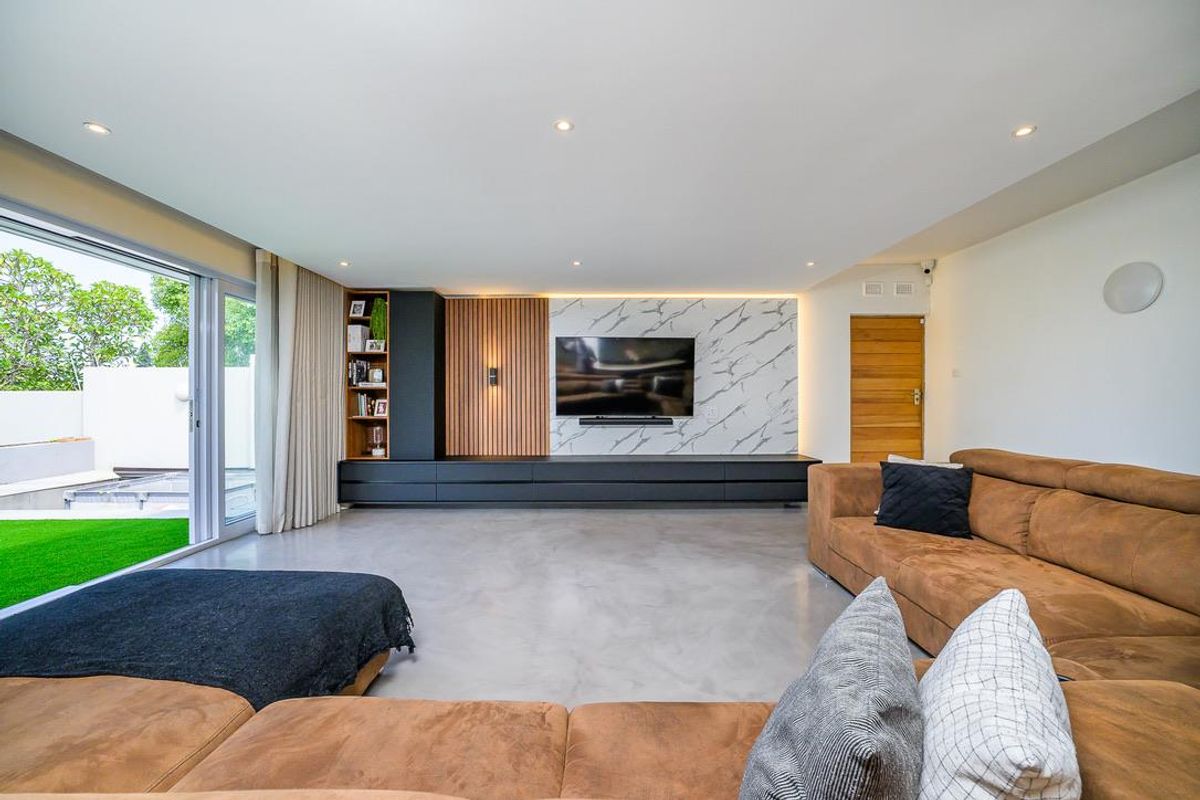 Modern living room featuring a custom built-in media wall with marble-look cladding, timber slat detailing, and integrated cabinetry, opening onto a private garden patio.