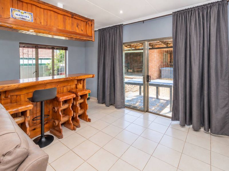 A dedicated bar area featuring a built-in wooden counter, tiled flooring, and direct access to an outdoor patio through sliding glass doors.