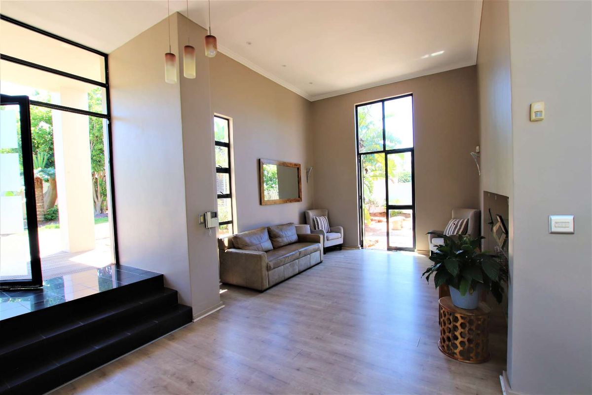 Spacious living room featuring high ceilings, laminate flooring, a built-in fireplace, and large black-framed glass doors providing access to the outdoor area.