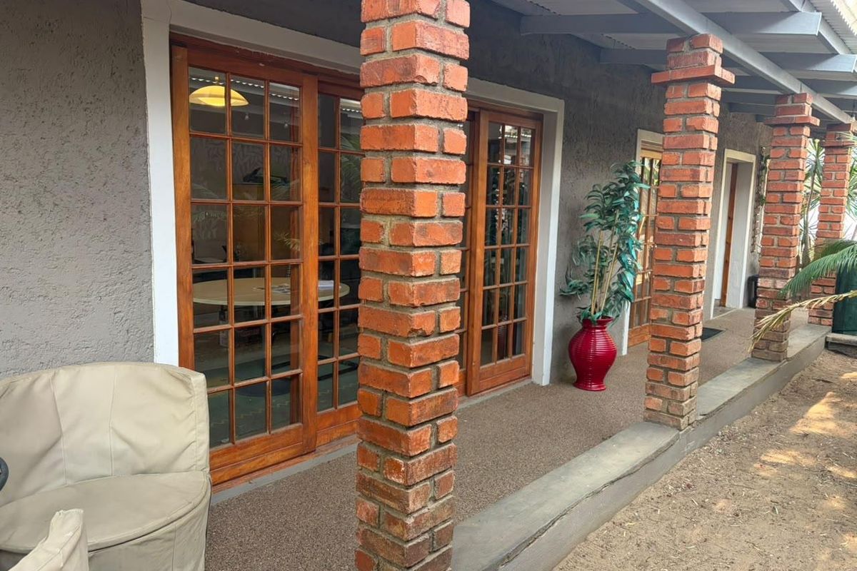 A covered patio area featuring exposed brick columns and wooden framed glass sliding doors providing access to the office interior.