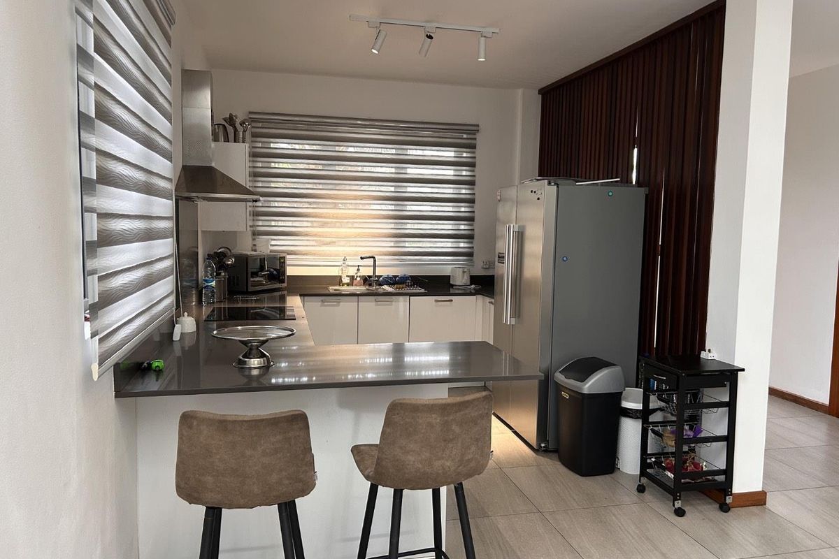 A modern kitchen featuring a U-shaped layout with dark countertops, white cabinetry, a stainless steel extractor fan, and tiled flooring.
