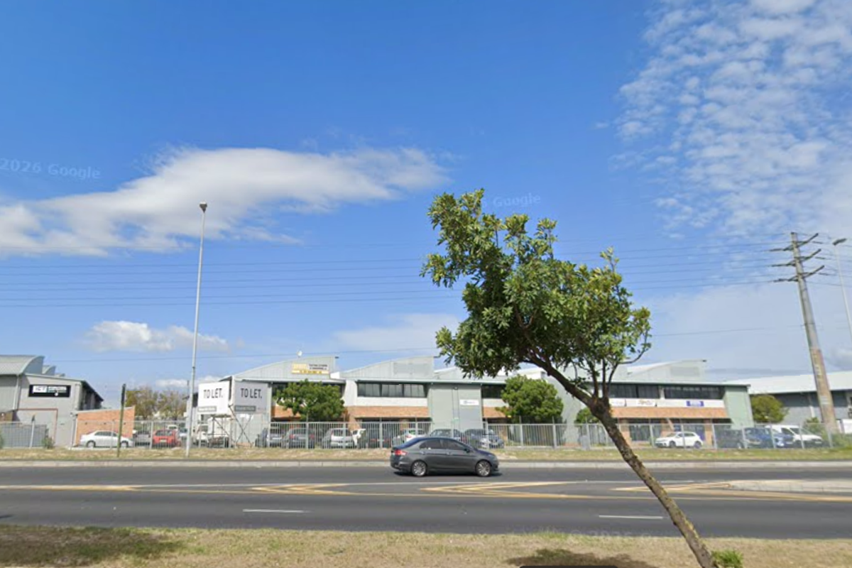 Street view of an industrial warehouse complex featuring metal perimeter fencing and clear road access.