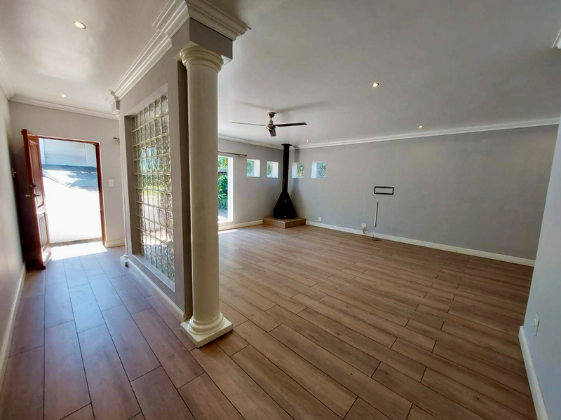 Spacious open-plan living area featuring wood-look tile flooring, a decorative column, glass block partition, and a built-in wood-burning fireplace.