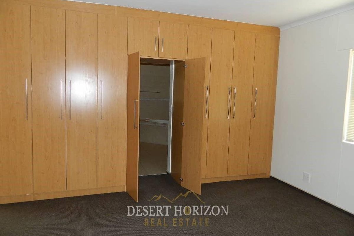 A bedroom featuring extensive floor-to-ceiling built-in wooden cabinetry with integrated storage and a doorway leading to an adjoining bathroom.