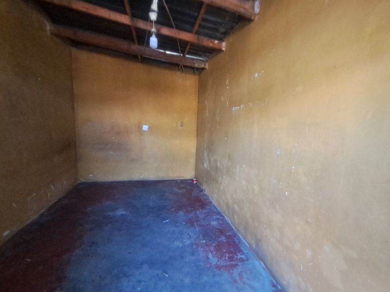 An empty utility space featuring exposed timber rafters, concrete flooring, and basic electrical infrastructure, suitable for storage or renovation.