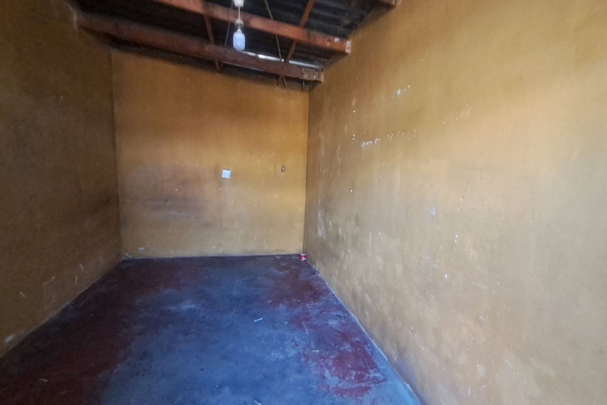 An empty utility space featuring exposed timber rafters, concrete flooring, and basic electrical infrastructure, suitable for storage or renovation.