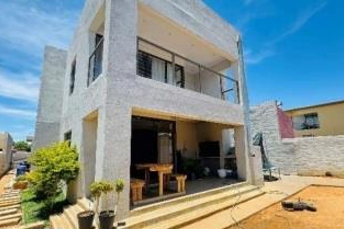A two-story residential property featuring a ground-floor patio and an upper-level balcony, set within a fenced yard with basic landscaping.