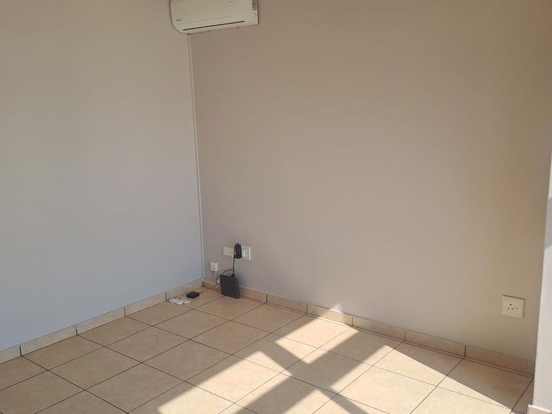 An empty living area featuring neutral tiled flooring, a ceiling fan, and a wall-mounted split-system air conditioning unit.