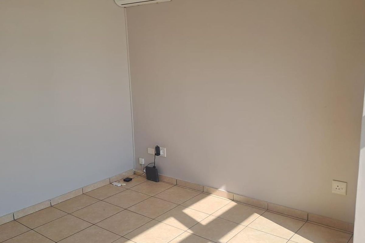An empty living area featuring neutral tiled flooring, a ceiling fan, and a wall-mounted split-system air conditioning unit.