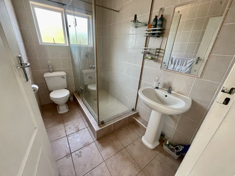 A functional bathroom featuring a pedestal basin, a glass-enclosed shower, and neutral wall and floor tiling.