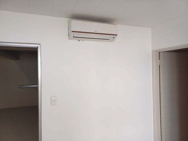 A clean, neutral interior space featuring a wall-mounted air conditioning unit and two doorways.
