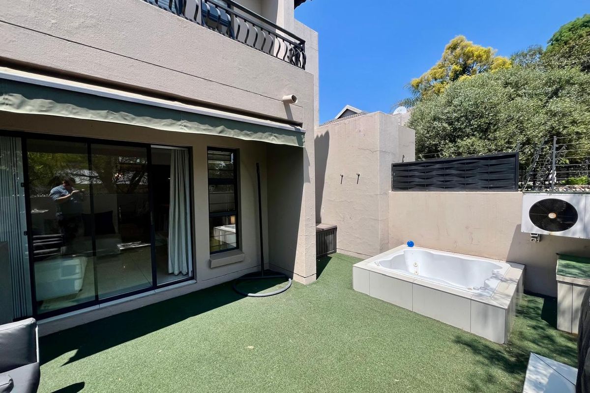 Rear courtyard featuring a built-in jacuzzi, artificial turf, and a retractable awning, providing a private outdoor entertainment space.