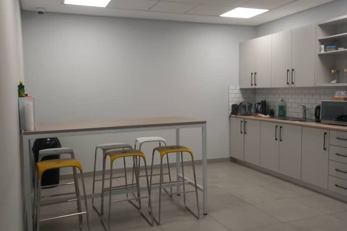 Modern office kitchenette featuring light grey cabinetry, subway tile backsplash, integrated sink, and recessed LED panel lighting with large format floor tiles.