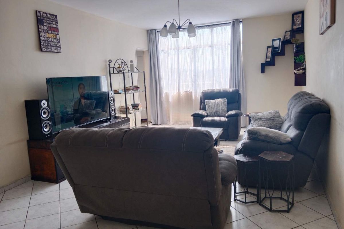 A comfortable living room featuring ceramic floor tiles, a central ceiling light fixture, and a large window that allows for natural light.