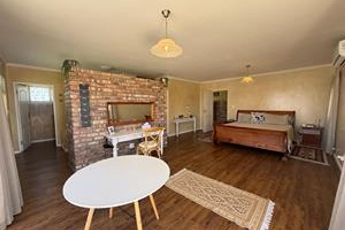 Spacious bedroom featuring an exposed brick feature wall, laminate flooring, and an integrated air conditioning unit.