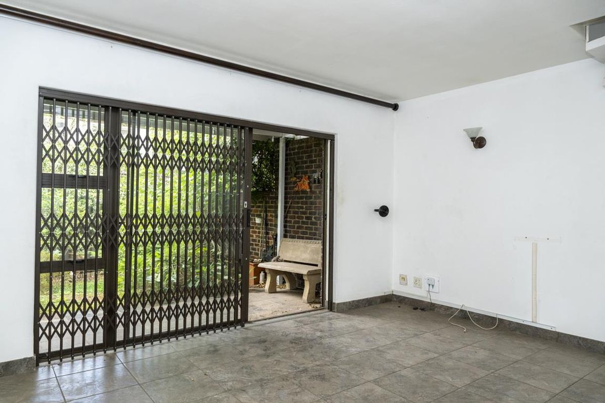 An empty living area featuring tiled flooring, a wall-mounted light fixture, and a sliding door with a security gate leading to a patio.
