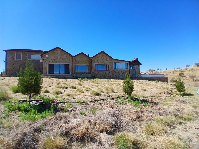 Rear view of a stone-clad small holding residence featuring multiple sliding glass doors and a pitched roof set against a rural landscape.